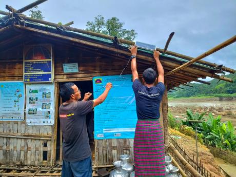 Two people install a solar kit on a village hut
